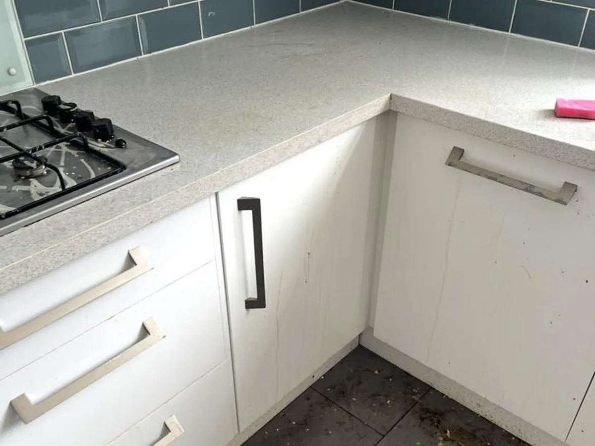A kitchen with marked units and a dirty floor before cleaning